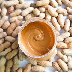 Open jar of creamy peanut butter surrounded by peanuts